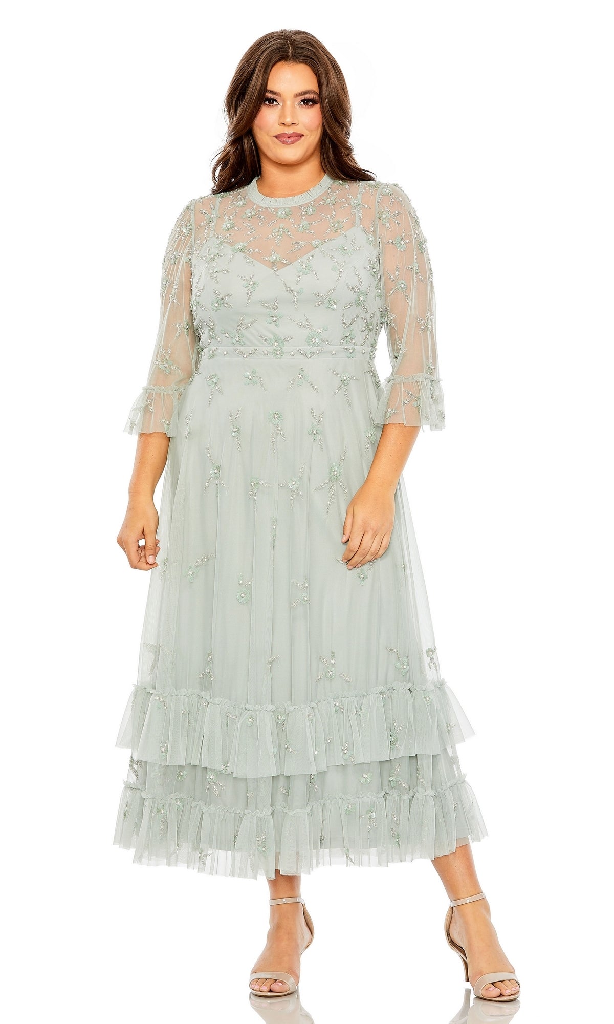 A woman wearing the Tea-Length Plus-Size Formal Dress 9263 by Mac Duggal—light green, long-sleeve, a-line with floral embroidery and tiered ruffle hem—paired with open-toe heels.